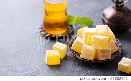 Turkish delight on a copper plate with glass of tea. Grey stone background. Copy space. Turkish delight on a copper plate with glass of tea. Grey stone background. Copy space. 62602831
