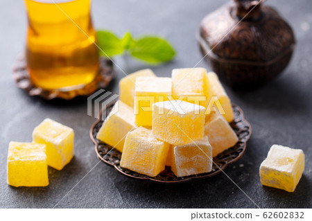 Turkish delight on a copper plate with glass of tea. Grey stone background. Close up. 62602832