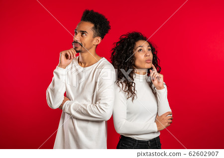 Portrait of young thinking pondering couple on red studio background. Man and woman look in different directions and everyone thinks about his problem. 62602907