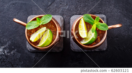 Cold Moscow Mules cocktail with ginger beer, vodka, lime and mint. Grey stone background. Top view. Cold Moscow Mules cocktail with ginger beer, vodka, lime and mint. Grey stone background. Top view. 62603121