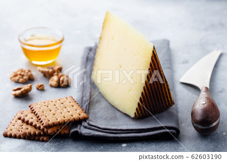 Hard cheese, Manchego with nuts, honey and crackers on grey background. Close up. Hard cheese, Manchego with nuts, honey and crackers on grey background. Close up. 62603190