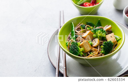 Soba noodles with vegetables and fried tofu in a bowl. Copy space. Grey background. Soba noodles with vegetables and fried tofu in a bowl. Copy space. Grey background. 62603334