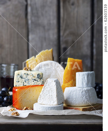 Cheese assortment: blue cheese, hard cheese, soft cheese on a parchment paper. Wooden background. Copy space. Cheese assortment: blue cheese, hard cheese, soft cheese on a parchment paper. Wooden background. Copy space. 62603539