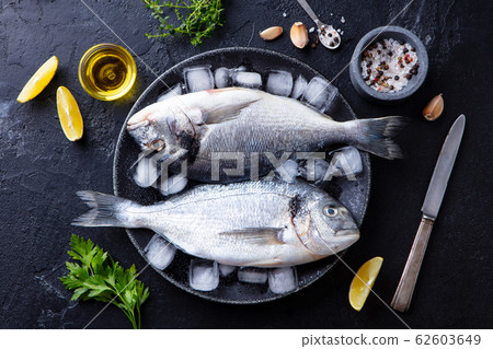 Dorado raw fish on a plate with ice and lemon. Black slate background. Top view. 62603649