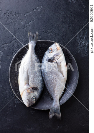 Raw fish dorado on a plate. Black stone background. Top view. 62603661