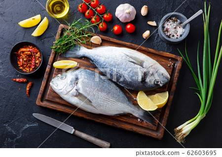 Raw fish Dorado on a wooden cutting board with vegetables, herbs and spices. Black stone background. Top view. 62603695