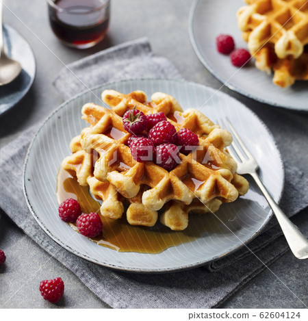 Breakfast Belgian waffles with maple syrup and fresh raspberry. Grey background. Breakfast Belgian waffles with maple syrup and fresh raspberry. Grey background. 62604124
