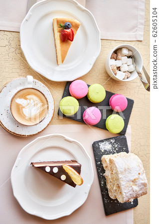 Breakfast in the cafe, morning coffee. Cappuccino and lots of desserts on the table. Napoleon, chocolate cake, cheesecake and macaroons. 62605104