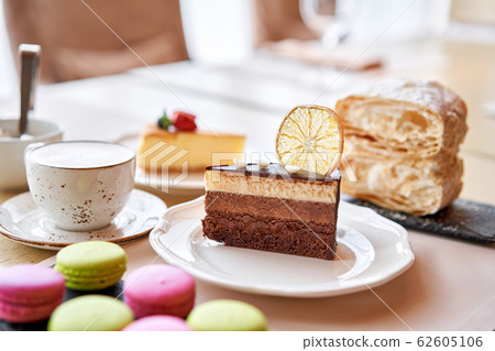 Chocolate sponge cake, with mousse, decorated with Orange slice and meringue. Breakfast in the cafe, morning coffee. on wooden table. Chocolate sponge cake, with mousse, decorated with Orange slice and meringue. Breakfast in the cafe, morning coffee. on wooden table. 62605106