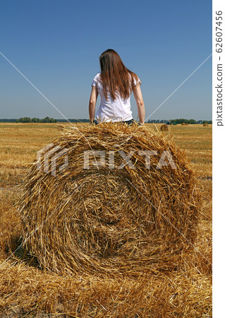 Young woman sitting on the straw bale in field 62607456