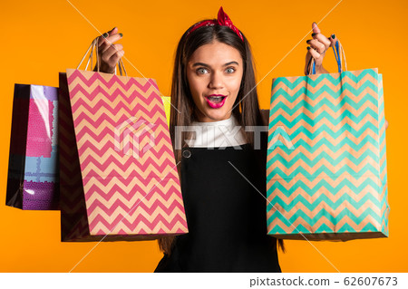 Happy young woman with long hair with paper bags after shopping isolated on yellow studio background. Seasonal sale, purchases, spending money on gifts concept 62607673