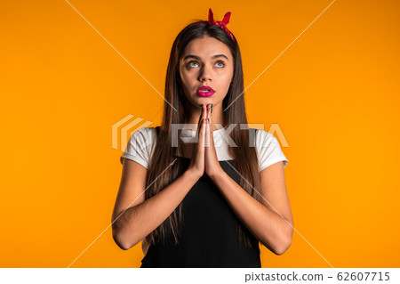Cute young girl with beautiful hairstyle praying over yellow background. Woman begging someone. 62607715