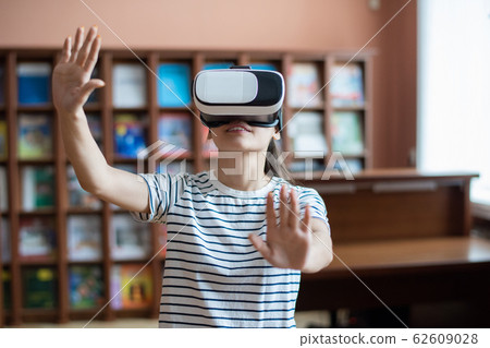 Contemporary teenage girl with vr headset touching virtual display 62609028