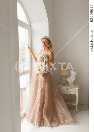 Young bride in a beautiful dress and wreath on her head holding a bouquet of flowers in bright white studio. Wedding concept. Young bride in a beautiful dress and wreath on her head holding a bouquet of flowers in bright white studio. Wedding concept. 62609655