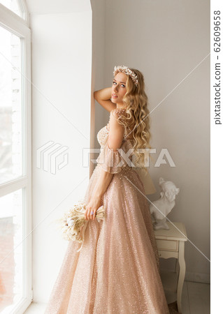 Young bride in a beautiful dress and wreath on her head holding a bouquet of flowers in bright white studio. Wedding concept. Young bride in a beautiful dress and wreath on her head holding a bouquet of flowers in bright white studio. Wedding concept. 62609658