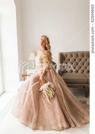 Young bride in a beautiful dress and wreath on her head holding a bouquet of flowers in bright white studio. Wedding concept. Young bride in a beautiful dress and wreath on her head holding a bouquet of flowers in bright white studio. Wedding concept. 62609660