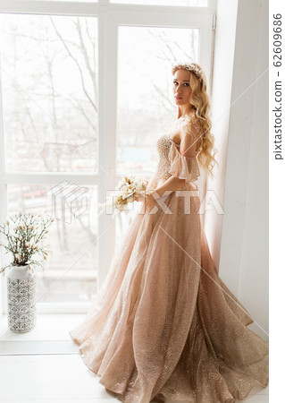 Young bride in a beautiful dress and wreath on her head holding a bouquet of flowers in bright white studio. Wedding concept. 62609686