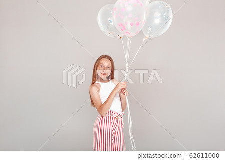 Inclusive Beauty. Girl with freckles standing isolated on grey holding balloons posing smiling happy 62611000