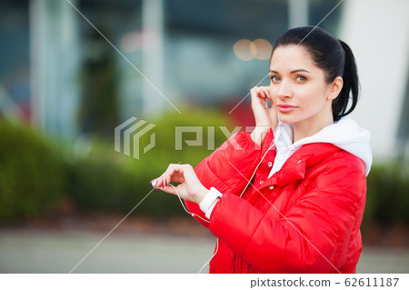 Photo of Joyful Fitness Woman 30s in Sportswear Touching Bluetooth Earpod and Holding Mobile Phone, While Resting in Green Park 62611187
