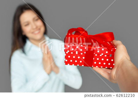 Freestyle. Young woman standing isolated on grey getting present from man close-up burred Freestyle. Young woman standing isolated on grey getting present from man close-up burred 62612210