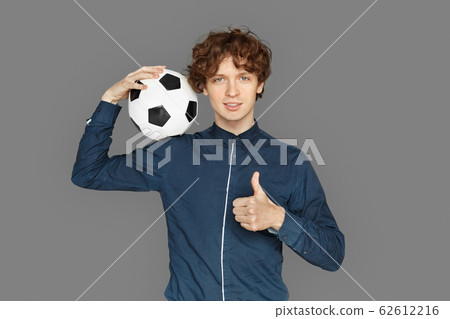 Sporty Lifestyle. Teenager boy standing isolated on grey with soccer ball showing thumb up smiling positive 62612216