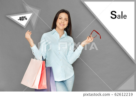 Freestyle. Young woman standing isolated on grey with shopping bags holding sunglasses joyful Freestyle. Young woman standing isolated on grey with shopping bags holding sunglasses joyful 62612219