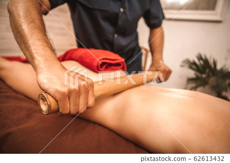 Alternative Medicine. Woman lying while therapist doing bamboo massage rolling on back close-up concentrated Alternative Medicine. Woman lying while therapist doing bamboo massage rolling on back close-up concentrated 62613432