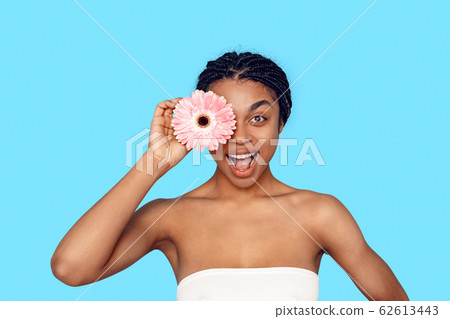 Beauty Concept. Young african woman isolated on blue covering eye with flower smiling excited 62613443
