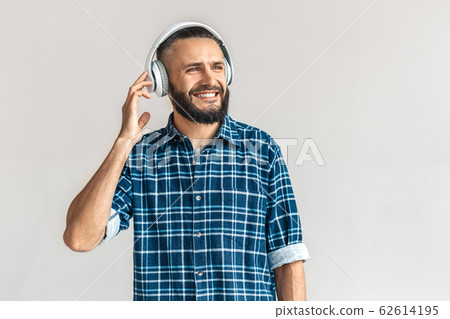 Freestyle. Guy wearing headphones in checkered shirt standing isolated on white listening music looking aside cheerful Freestyle. Guy wearing headphones in checkered shirt standing isolated on white listening music looking aside cheerful 62614195
