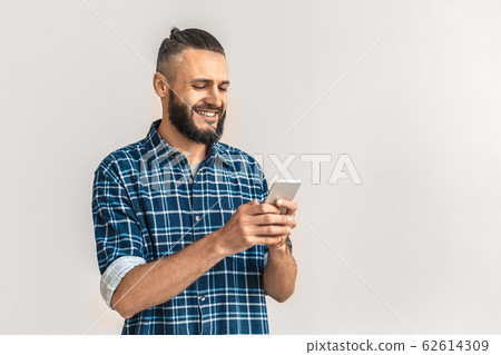 Freestyle. Guy in checkered shirt standing isolated on white chatting on smartphone smiling cheerful 62614309