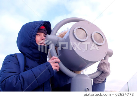 Mom and son looking through binoculars on roof of building in city in winter. 62624778