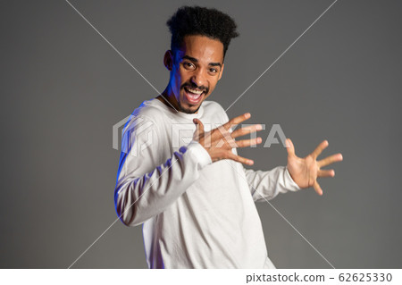 Young very active and energetic african american man in white wear smiling and dancing in good mood on grey background Young very active and energetic african american man in white wear smiling and dancing in good mood on grey background 62625330