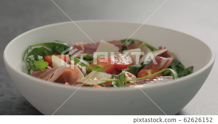 spices fall over salad with prosciutto, cherry tomatoes and mixed salad leaves in white bowl spices fall over salad with prosciutto, cherry tomatoes and mixed salad leaves in white bowl 62626152