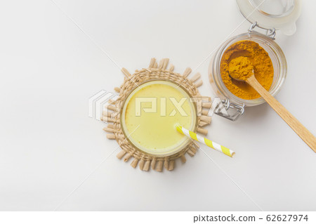 A glass jar filled with turmeric powder and cup of hot milk A glass jar filled with turmeric powder and cup of hot milk 62627974