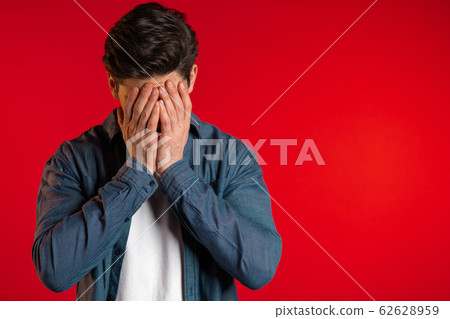 Young guy covers his face with hand from fatal disappointment, failure. Depressed lost man in shirt. Drama, emotions concept 62628959