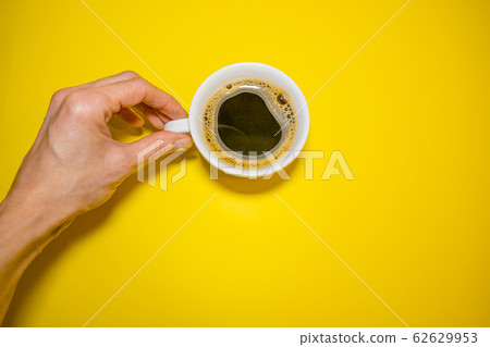 Female hand holding a white coffee Cup on a yellow background  62629953
