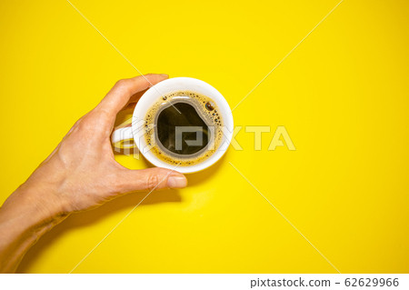 Female hand holding a white coffee Cup on a yellow background Female hand holding a white coffee Cup on a yellow background 62629966