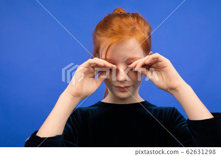 girl rubs her eyes due to dryness on a blue background girl rubs her eyes due to dryness on a blue background 62631298