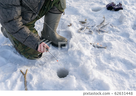 Winter fishing. Fisherman through the hole on the ice, fishing on a frozen pond 62631448
