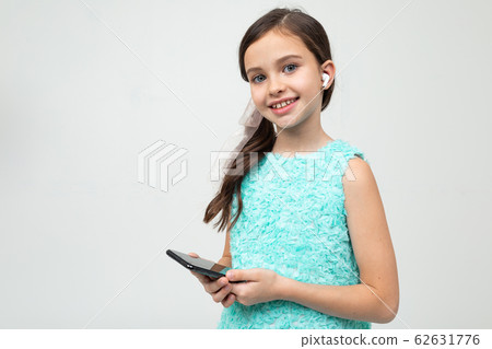 girl with headphones in her ears and a phone in her hands on a white background with copy space 62631776