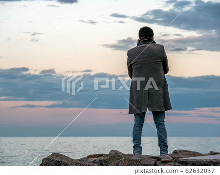 A man stands on the stones and looks at the sea at sunset 62632037