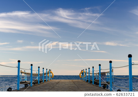 wooden platform with blue posts with ropes and orange lifebuoys on the background of the sea and sky with clouds 62633721
