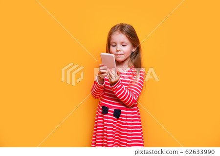Photo of pretty small girl holding telephone hands making new instagram post on yellow background Photo of pretty small girl holding telephone hands making new instagram post on yellow background 62633990