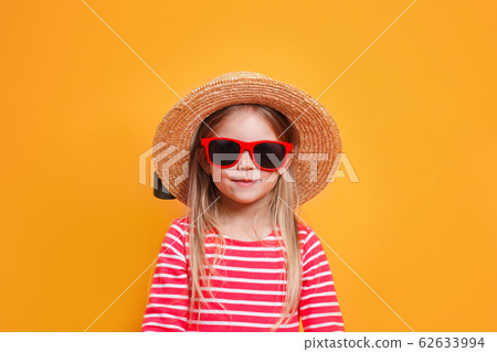 Fashionable little girl wearing a straw hat and sunglasses on yellow background Fashionable little girl wearing a straw hat and sunglasses on yellow background 62633994
