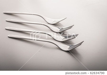 Many shiny gourmet restaurant quality design silver forks laying elegant in a row on a white dining table with copyspace - Concept of dinning cutlery, culinary silverware and food industry 62634790