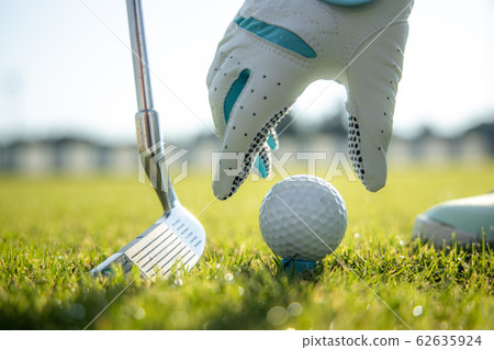 Hand in glove placing golf ball on tee 62635924