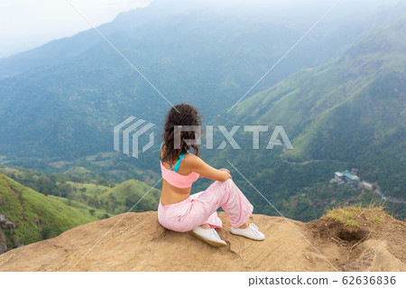 Girl enjoys a mountain view while standing on a Girl enjoys a mountain view while standing on a 62636836