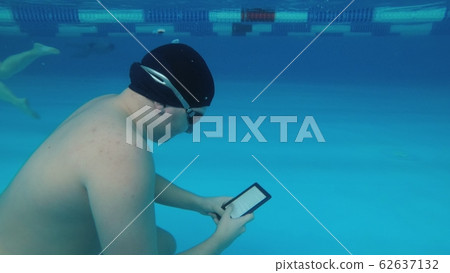 The guy is reading an electronic book underwater. The guy is reading an electronic book underwater. 62637132