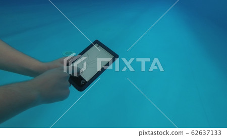 The guy is reading an electronic book underwater. The guy is reading an electronic book underwater. 62637133