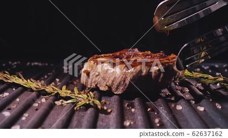 Delicious juicy meat steak cooking on grill. Aged prime rare roast grilling marble beef. Electric roaster, rosemary black pepper, salt. Kitchen tongs. Delicious juicy meat steak cooking on grill. Aged prime rare roast grilling marble beef. Electric roaster, rosemary black pepper, salt. Kitchen tongs. 62637162